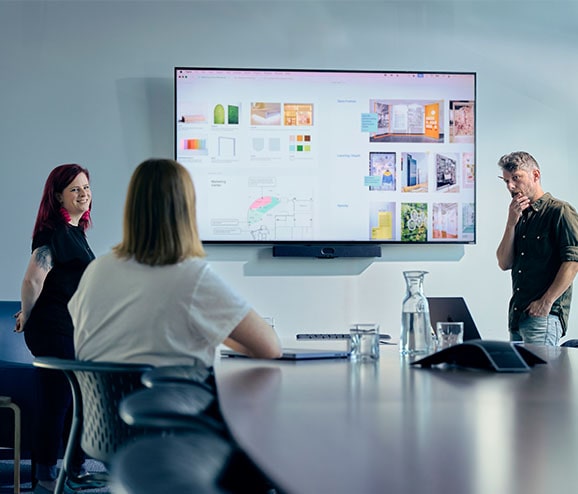 A white man with a beard and a white woman with red hair present a digital mood board, listening to a woman with her back to the camera.