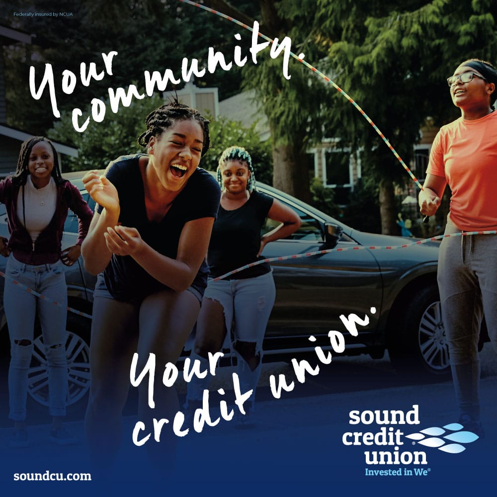 An ad features several young Black women playing jump rope on a sidewalk. Handwritten text declares “Your community. Your credit union.”